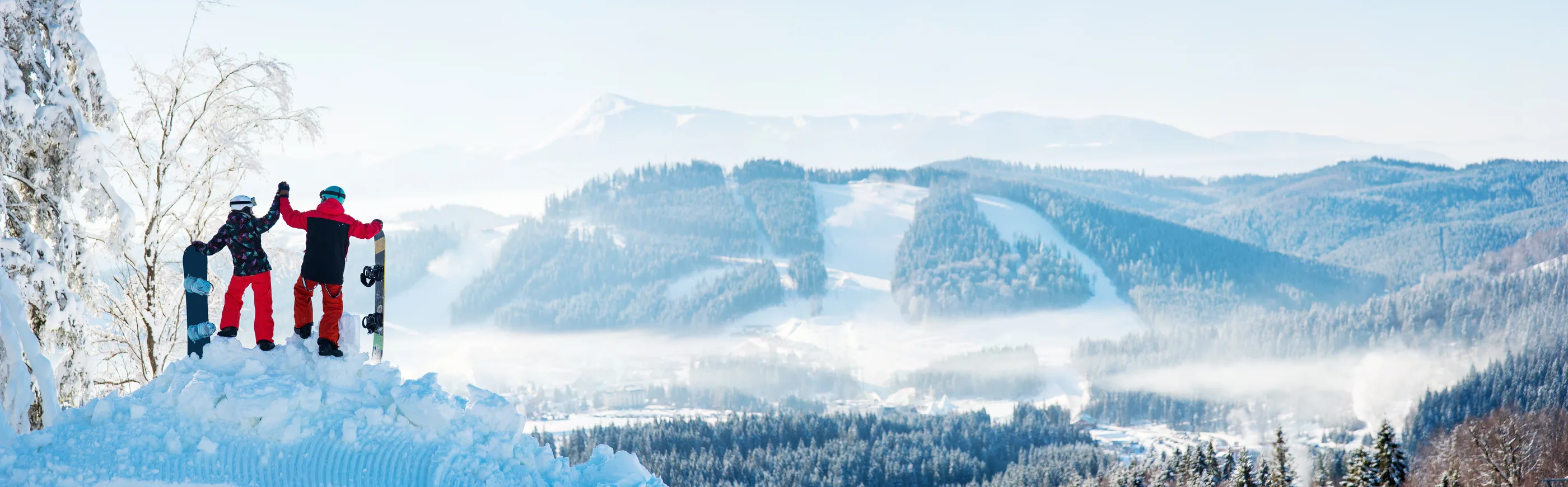 Two snowboarders celebrating atop a snowy mountain ridge.